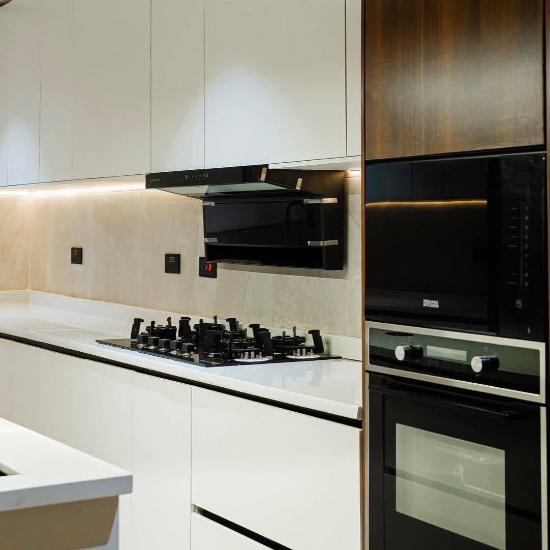 A modern handleless kitchen in white and warm wood with black integrated appliances and stone worktops