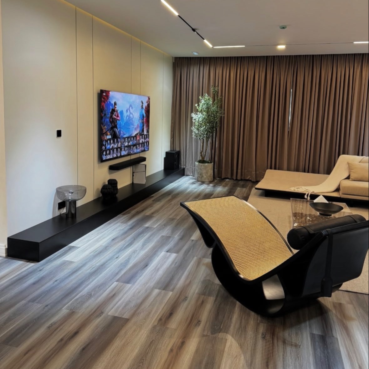 A warm media lounge with wood-panelled feature wall, floating black console, wood-look flooring and floor-to-ceiling drapery